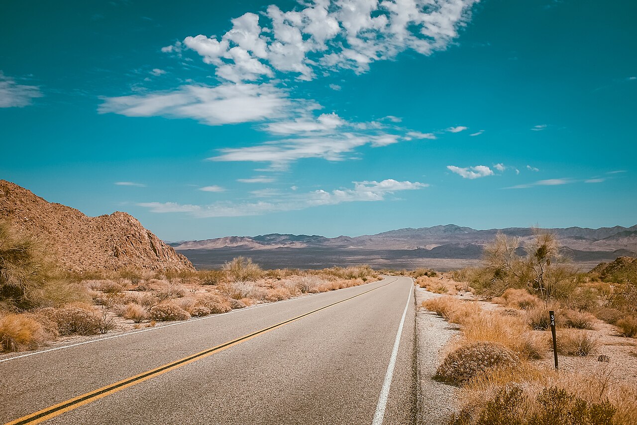 An empty highway stretching across the desert toward distant mountains